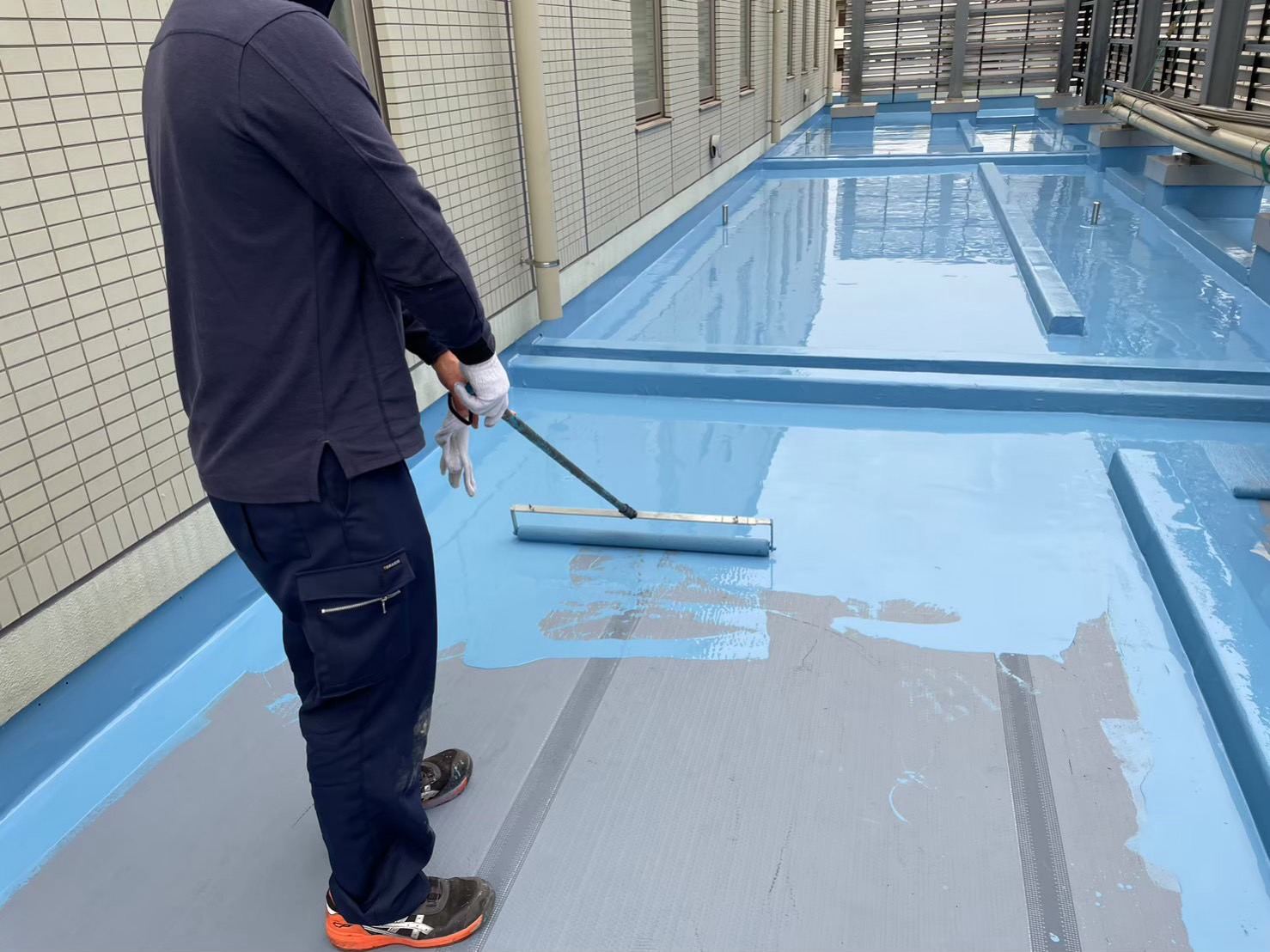 屋上に防水材をローラーで塗り広げている様子